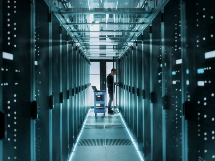 Corredor de data center com racks de servidores e técnico trabalhando ao fundo