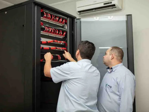 Técnicos da Ping organizando o cabeamento de um rack de rede com patch cords vermelhos
